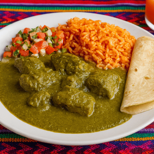 A plate of Tortuga en Verde with green herb sauce, red rice, pico de gallo, a warm tortilla, and an orange drink on a vibrant woven placemat.