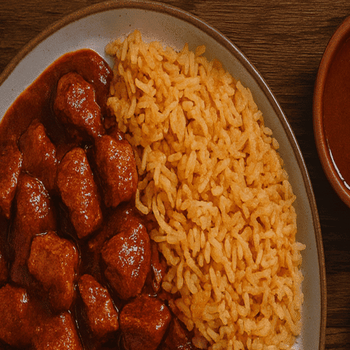 A rustic plate of Asado de Boda with tender pork chunks in red chile sauce, served with Mexican rice and lime on a wooden table.