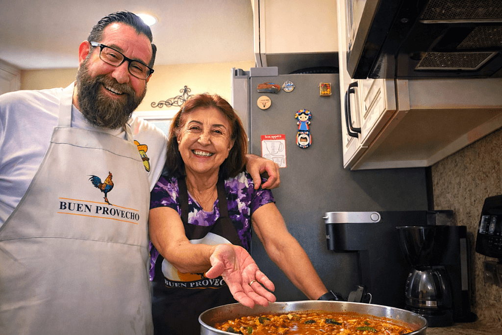 Man and his Mom serving homemade frijoles charros, a traditional Mexican cowboy bean stew, in a home kitchen.