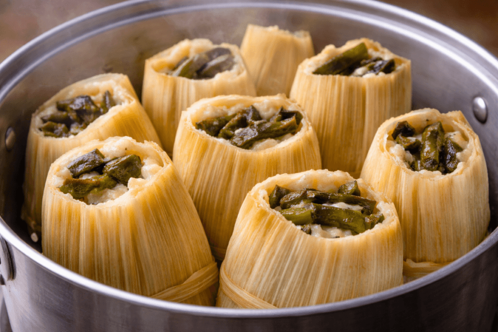 Tamales de rajas steaming in a metal pot, wrapped in corn husks and filled with roasted poblano peppers and melted cheese