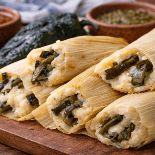 Tamales de rajas filled with roasted poblano peppers and melted cheese, unwrapped in corn husks and served on a rustic wooden board