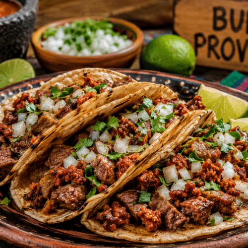 Campechano tacos filled with juicy steak and smoky Mexican chorizo topped with chopped onion and cilantro on a rustic plate with lime wedges and salsa in warm natural light.
