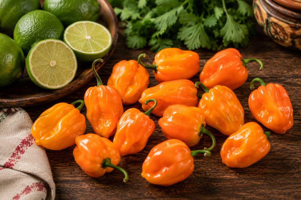 Fresh orange habanero peppers beside limes on a rustic wooden table