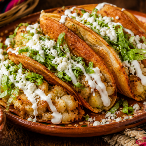 Crispy tacos de papa filled with seasoned potatoes and topped with shredded lettuce, queso fresco, Mexican crema, salsa verde, and lime.