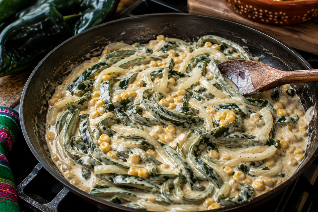 Rajas con crema cooking in a skillet with roasted poblano pepper strips, sliced onions, corn, Mexican crema, and melted cheese.